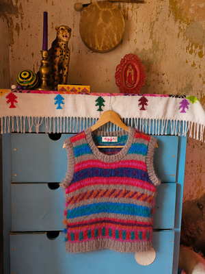 A colorful striped knit sweater vest hanging on a wooden hanger from a blue dresser in a rustic room. The vest features horizontal stripes of pink, blue, gray, and orange.